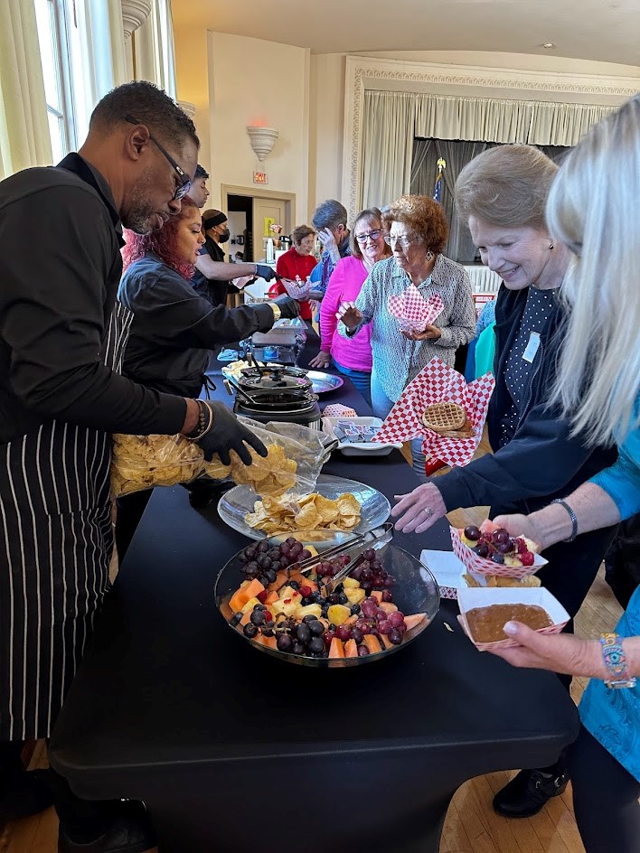 A group of people standing around a table with food.